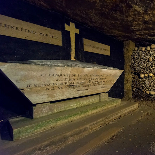 Underground view of the eerie Catacombs of Paris, with walls lined with skulls and bones.