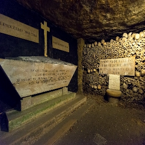 Underground view of the eerie Catacombs of Paris, with walls lined with skulls and bones.