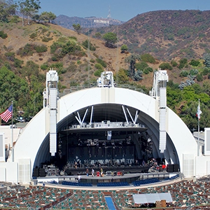 A panoramic view of the iconic Hollywood Bowl amphitheater during a live outdoor concert, with a vibrant audience and bright stage lights illuminating the night sky.